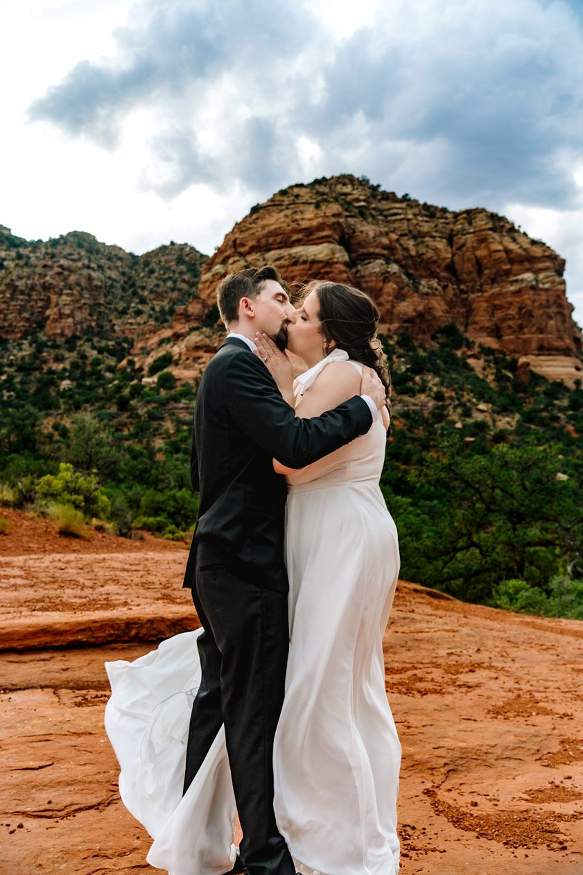 A romantic wedding kiss captured against the dramatic backdrop of Sedona's red rock cliffs.