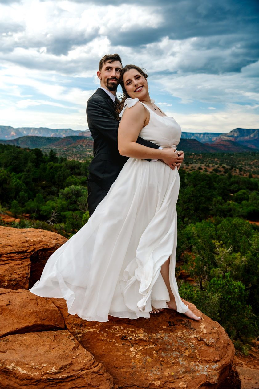 A dramatic wedding portrait on a cliff edge with Sedona's vast landscape in the background.