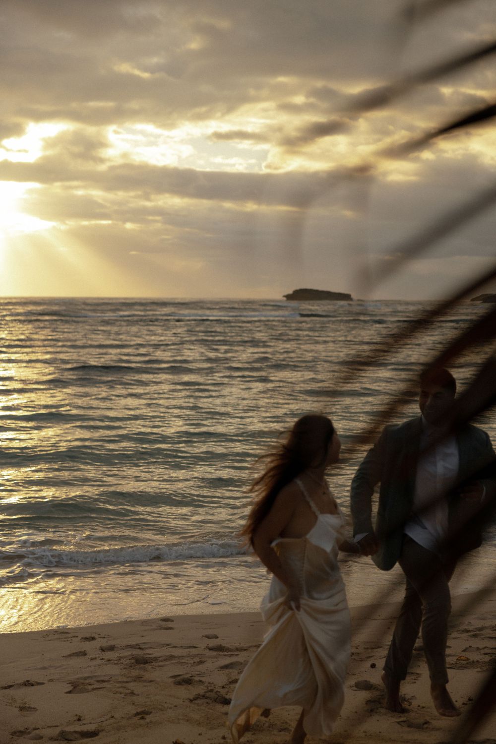 Silhouettes of a couple walking on the beach during golden hour with dramatic sunbeams breaking through clouds.