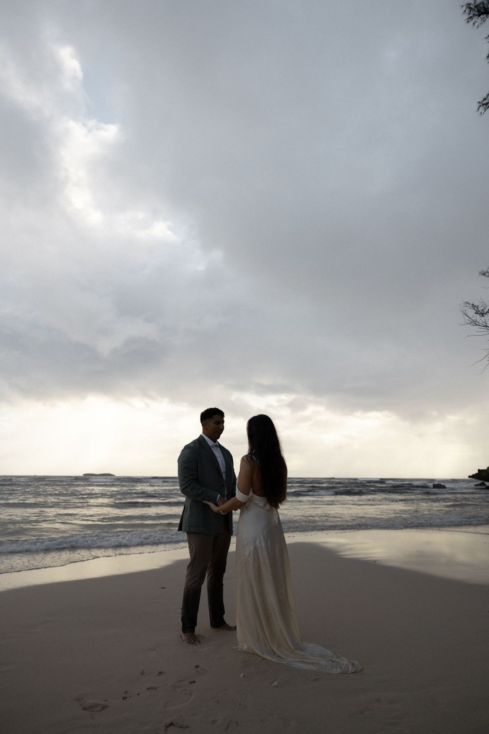 A couple stands together on a beach during sunset creating a romantic silhouette against the ocean.