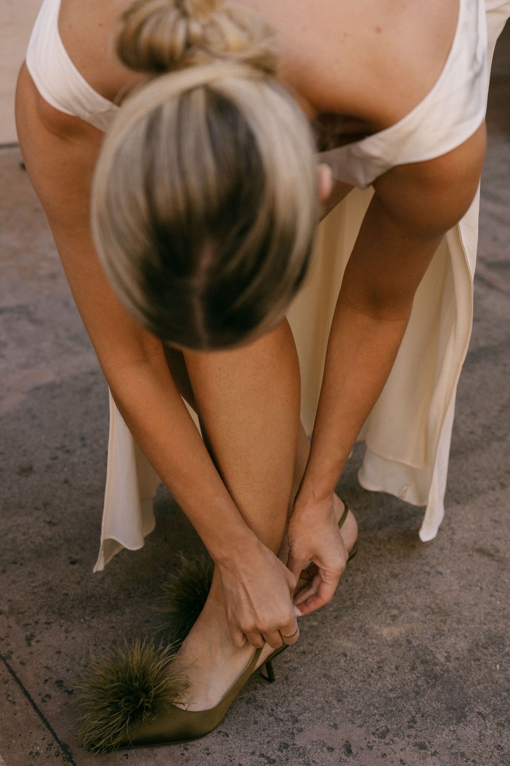 Close-up of hands fastening an elegant shoe with a feather detail.