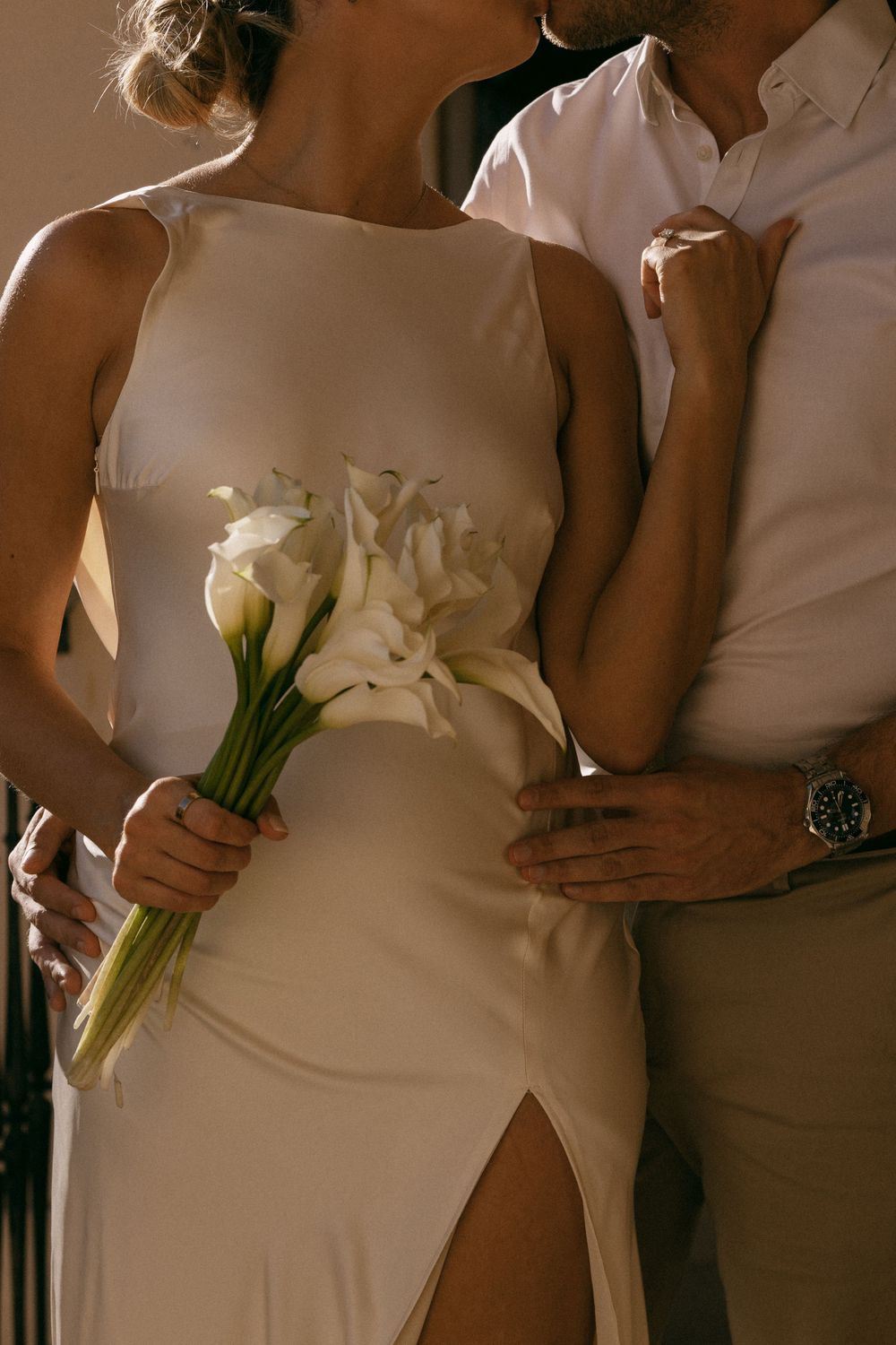 A close-up of a modern bride in a sleek white dress holding an elegant bouquet of white calla lilies.