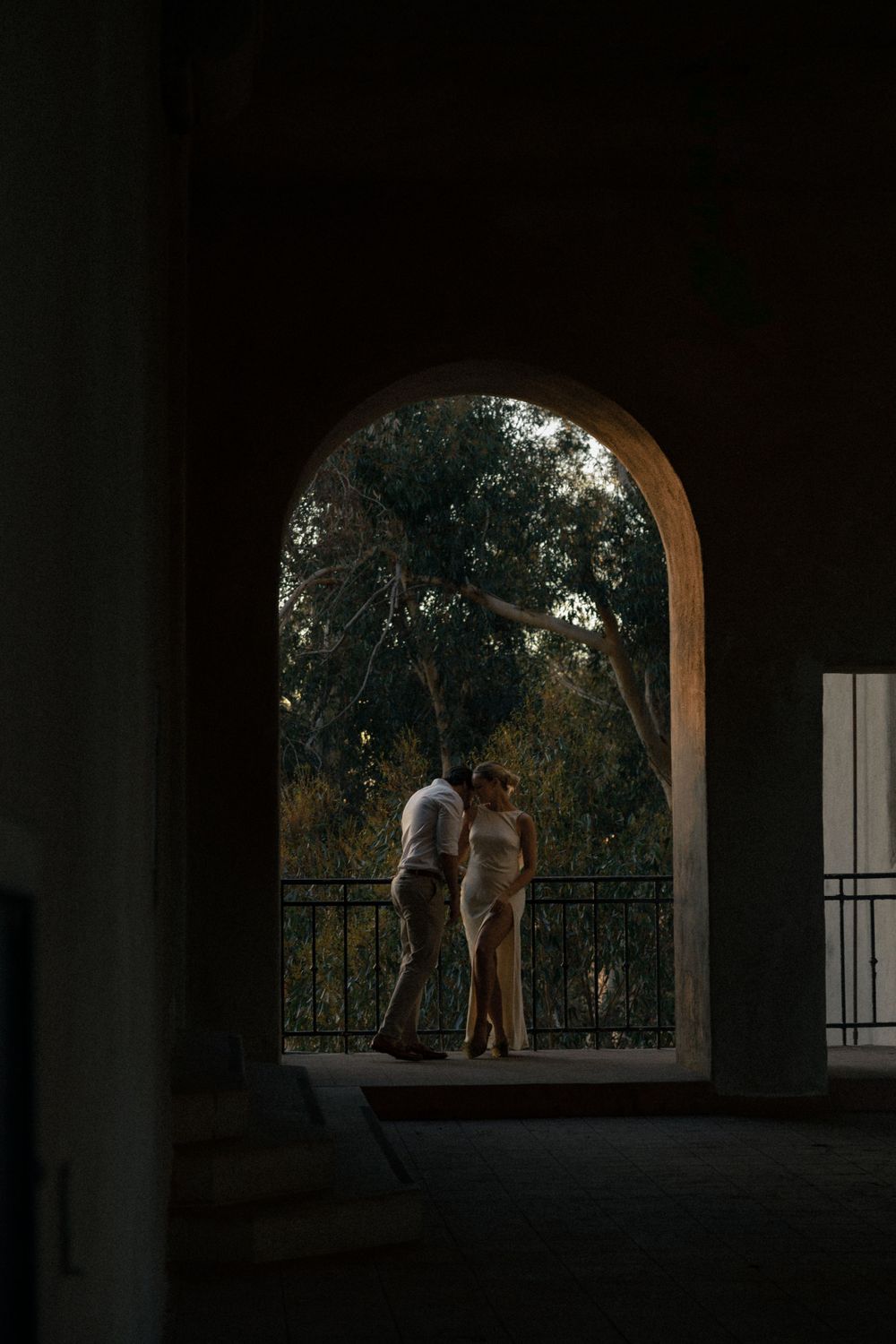 A silhouetted couple stands in an arched doorway during golden hour.