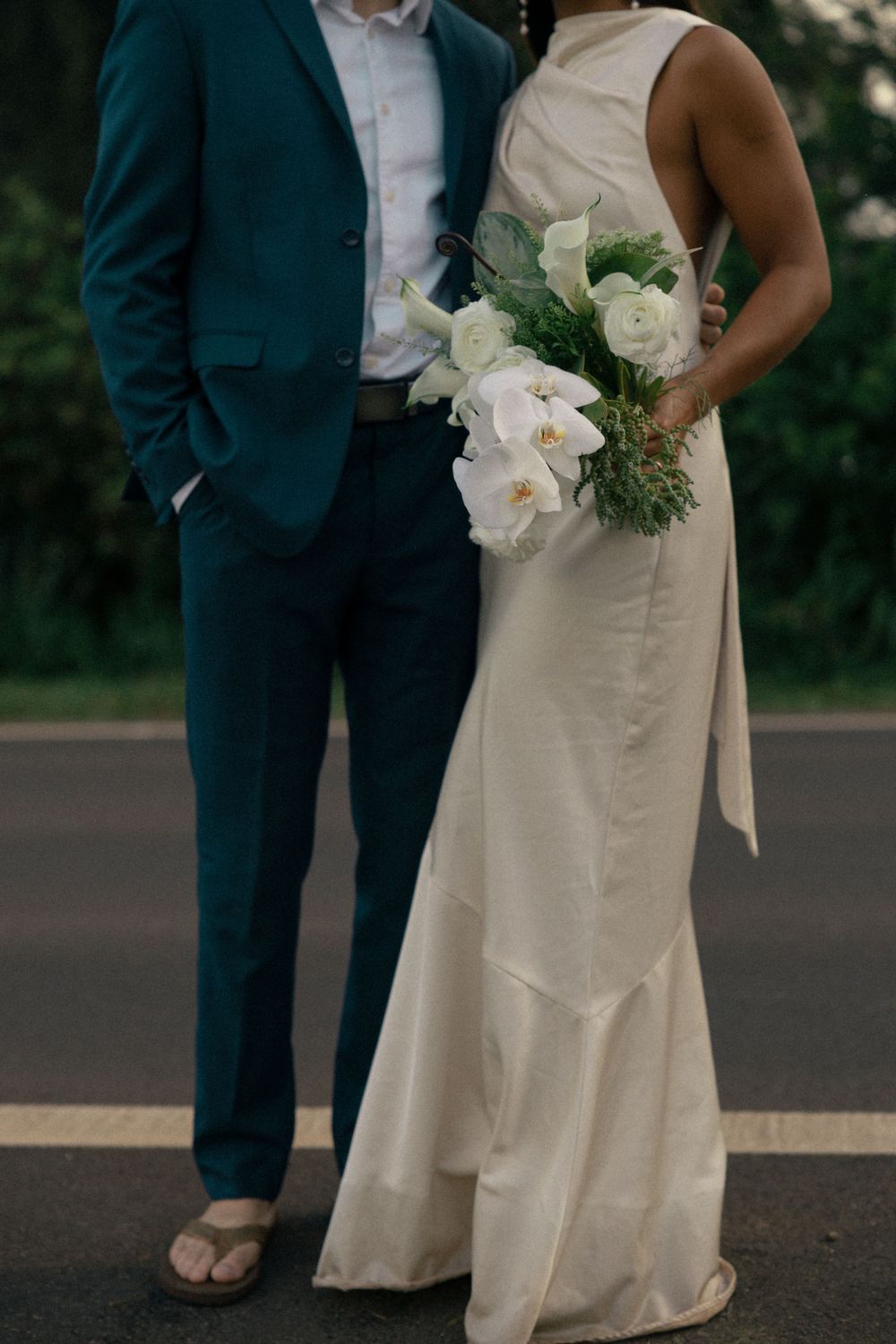 Elegant wedding attire detail with teal suit, white dress, and orchid bouquet.