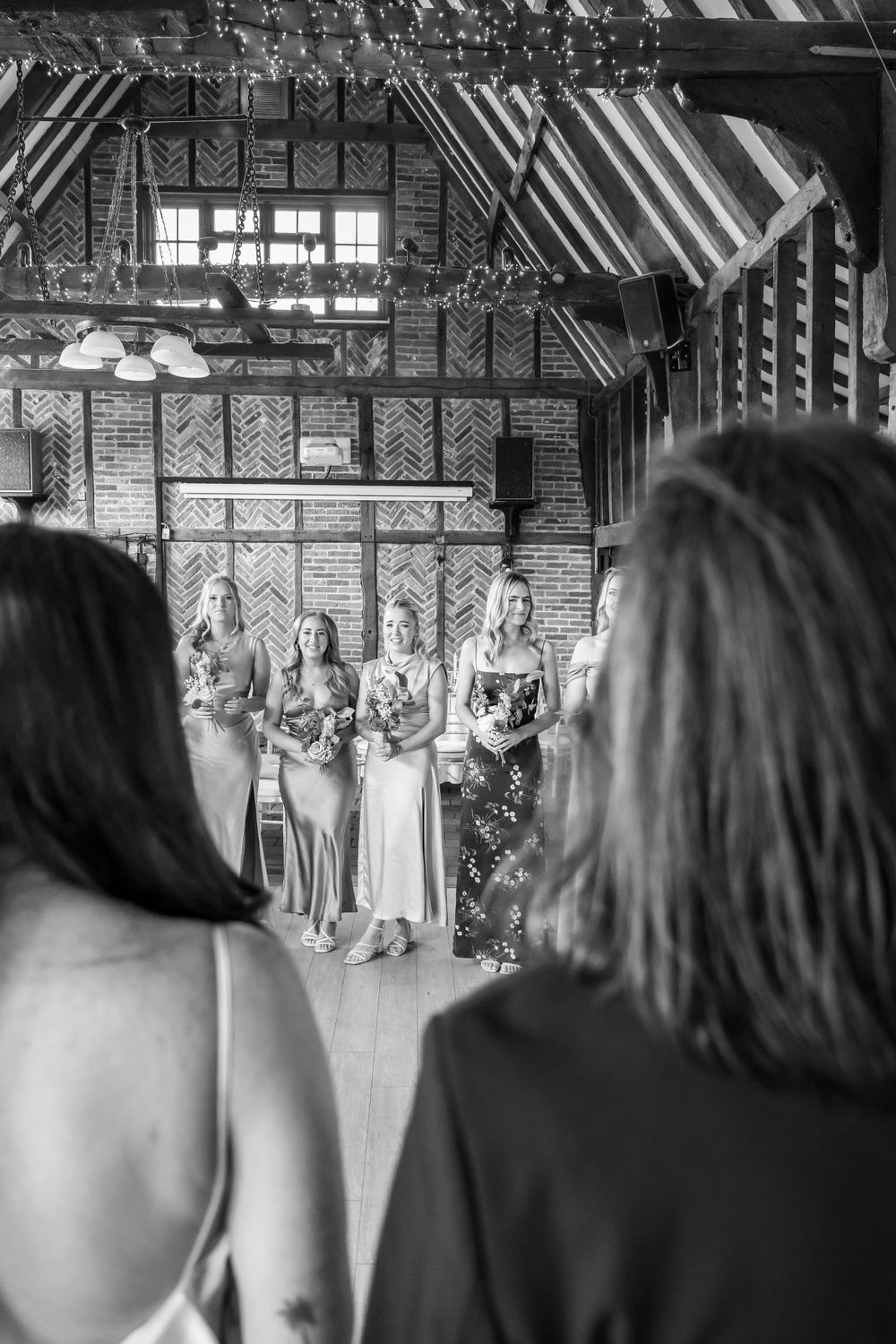 Black and white photo of wedding ceremony in historic brick building with wooden beams.