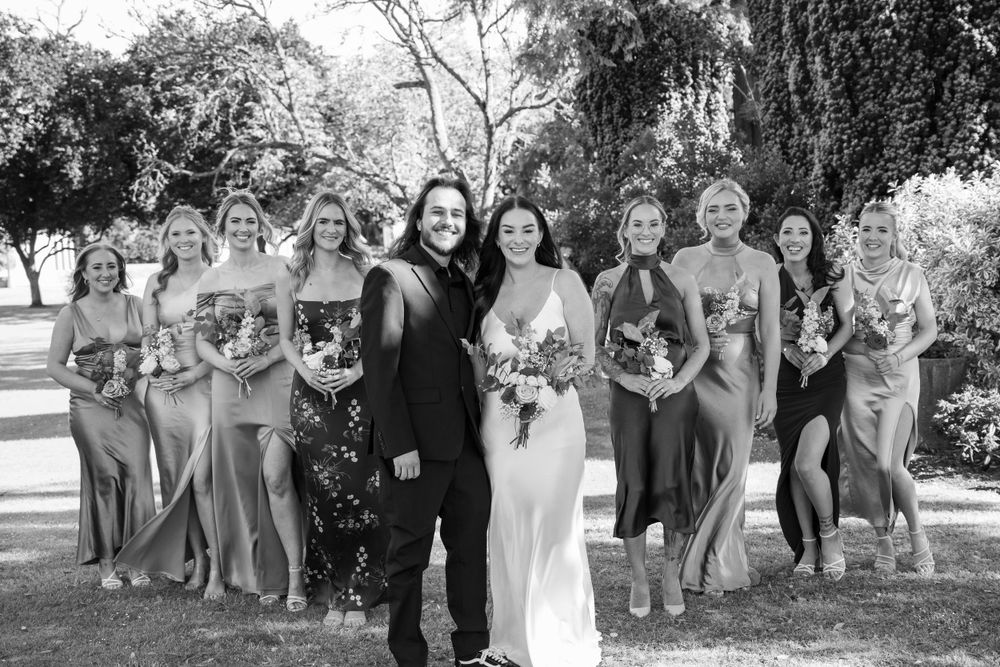 Black and white group portrait of wedding party gathered on garden lawn.