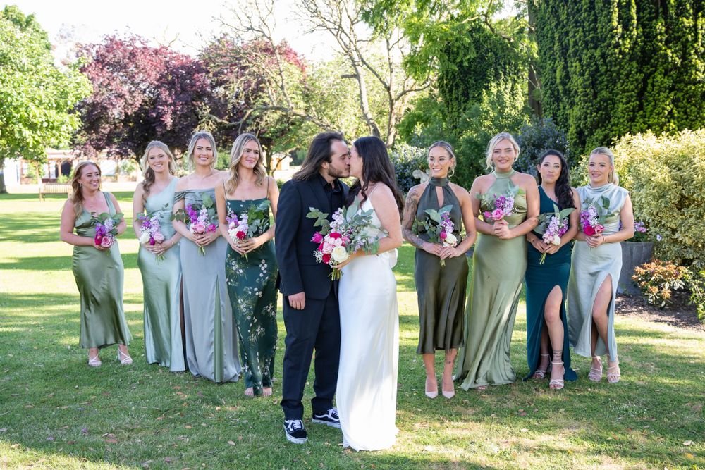 Wedding party assembles for cheerful group photo in blooming garden setting.