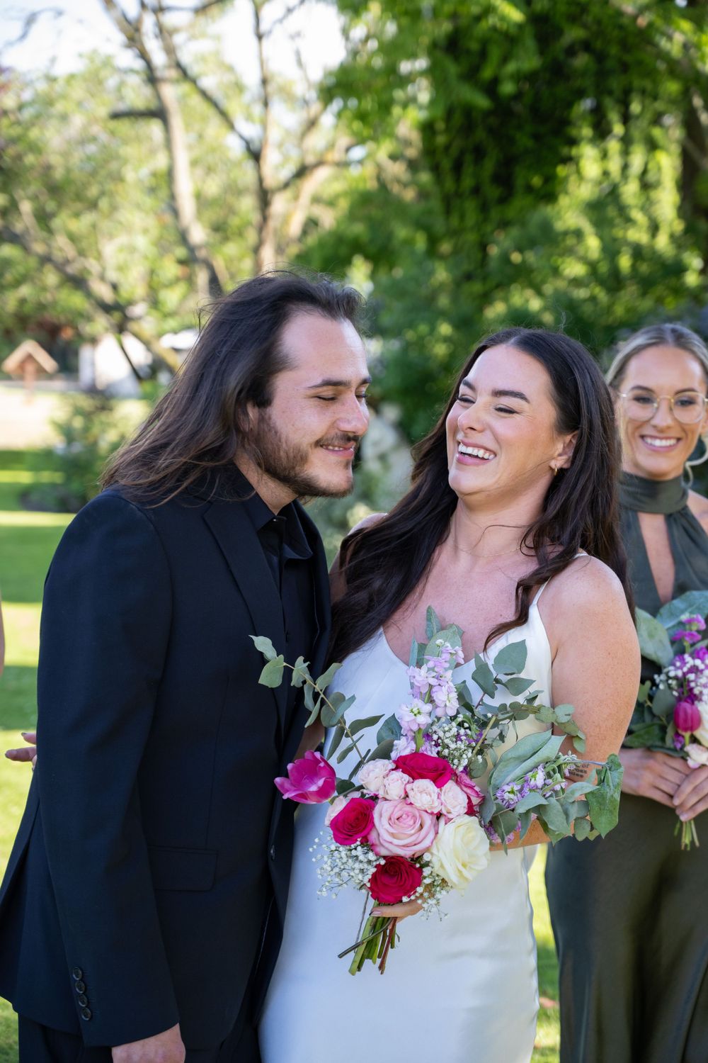 Happy couple shares joyful moment with bridal bouquet in sunny garden.