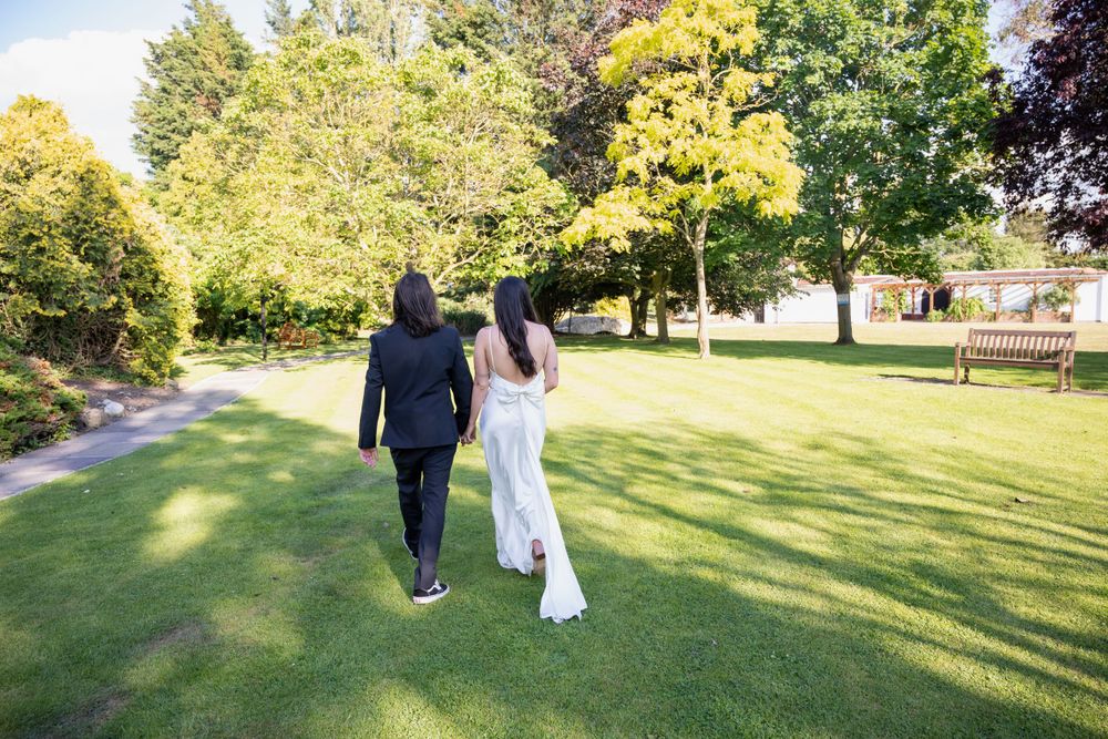 A couple walking hand in hand through a lush green park on a sunny day.