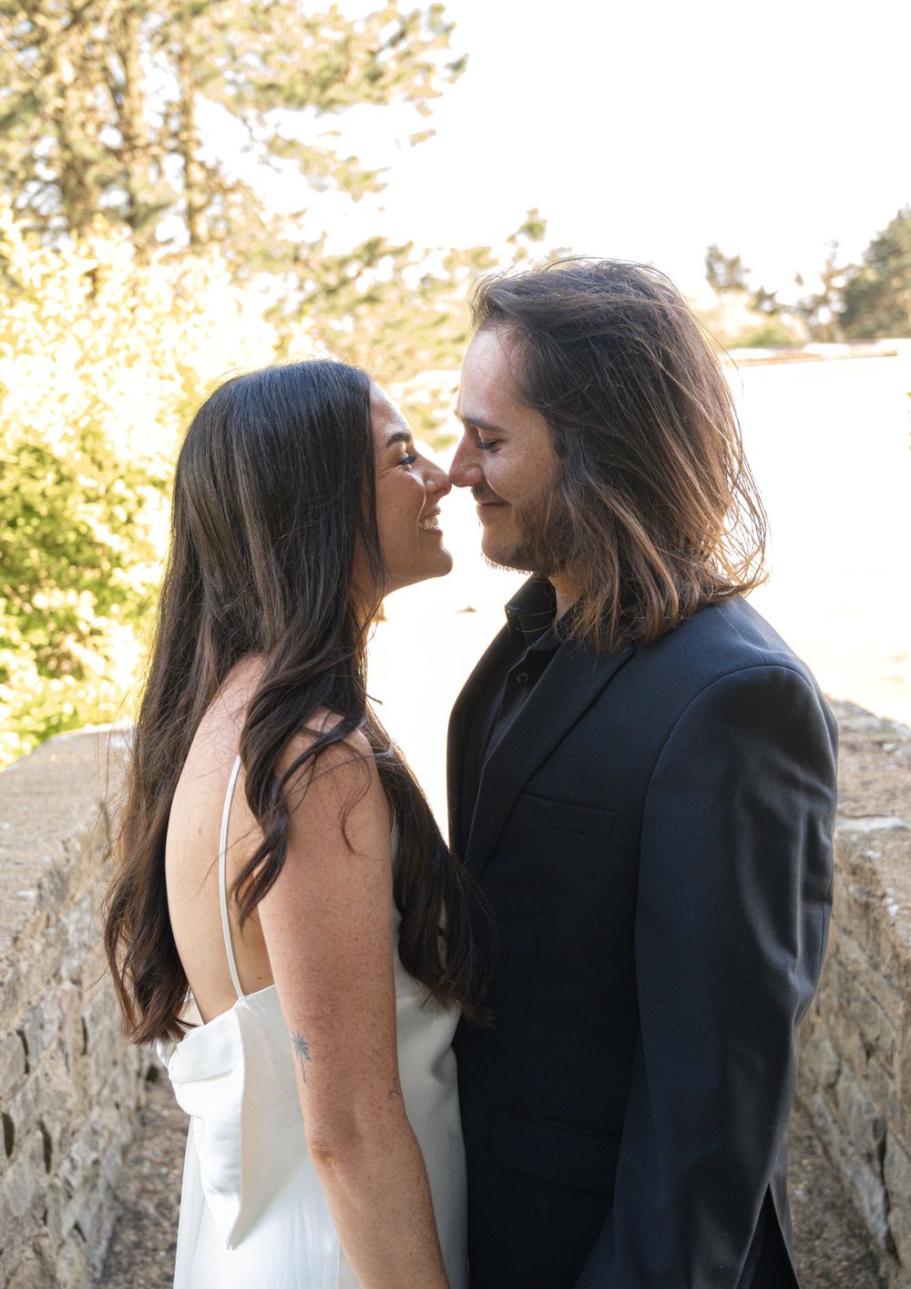 A romantic moment between a couple in formal attire against a sunlit natural backdrop.