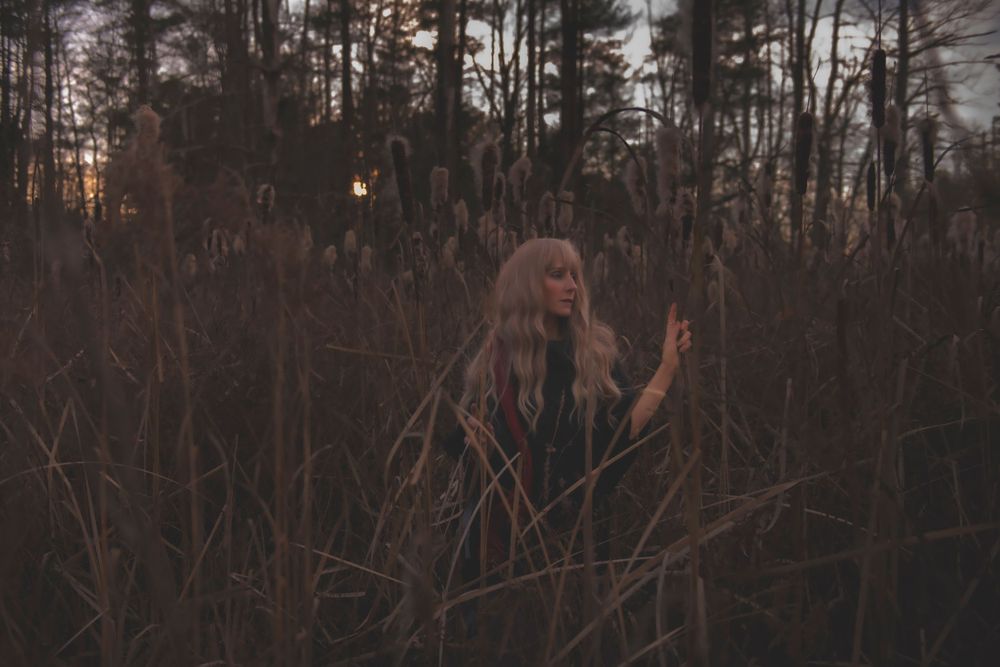 Ethereal figure with long hair among tall grasses and trees at twilight.