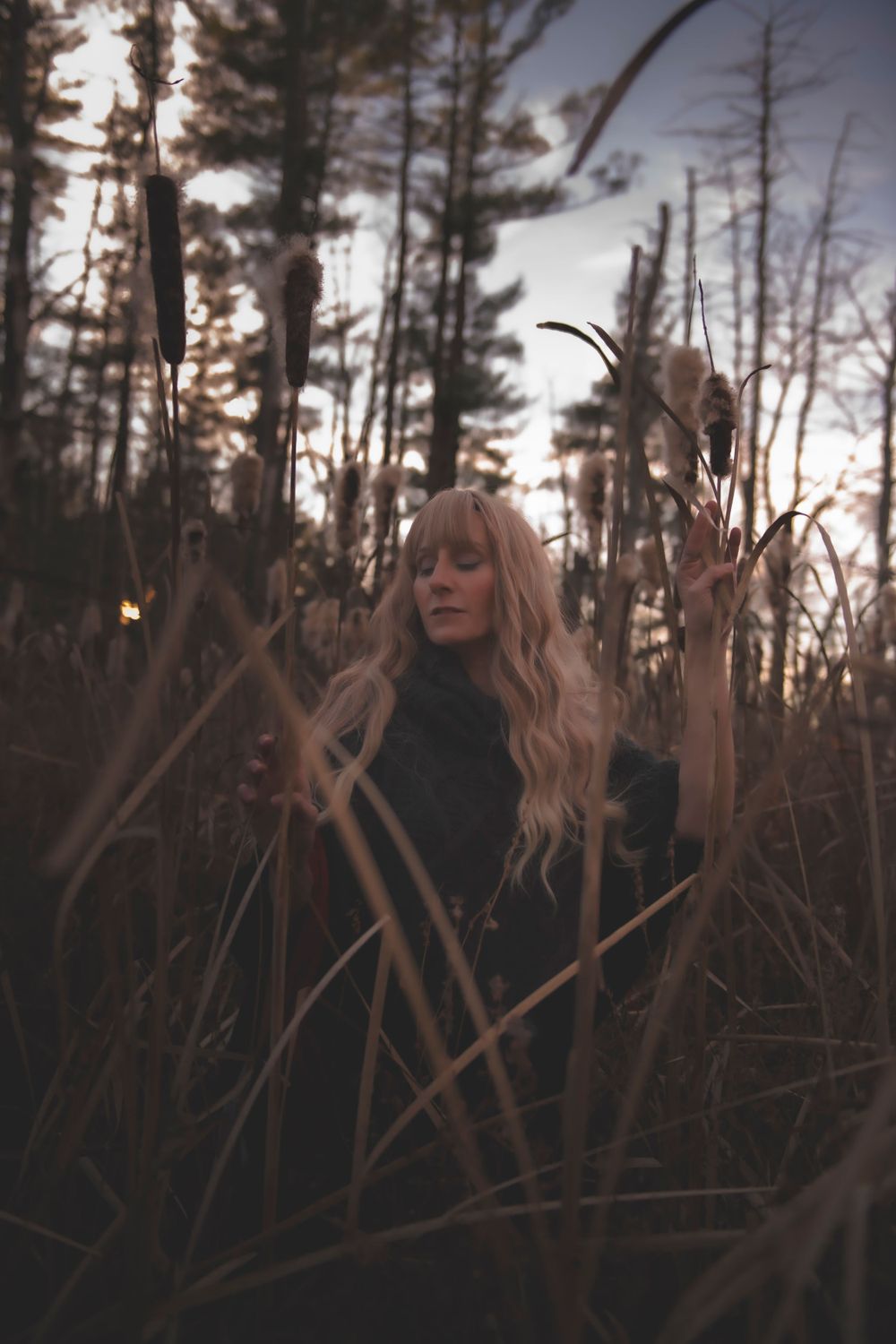 Moody portrait in autumn cattails featuring long wavy hair and dark turtleneck.