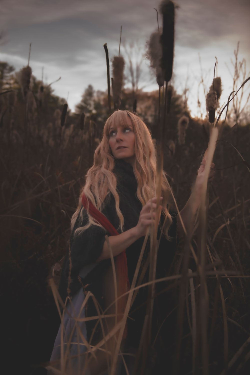 Dramatic shot among cattails showing flowing hair and dark clothing with red accent.