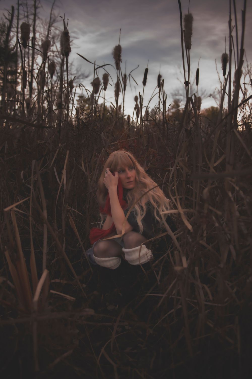 Artistic pose among tall cattail reeds at dusk with moody lighting.