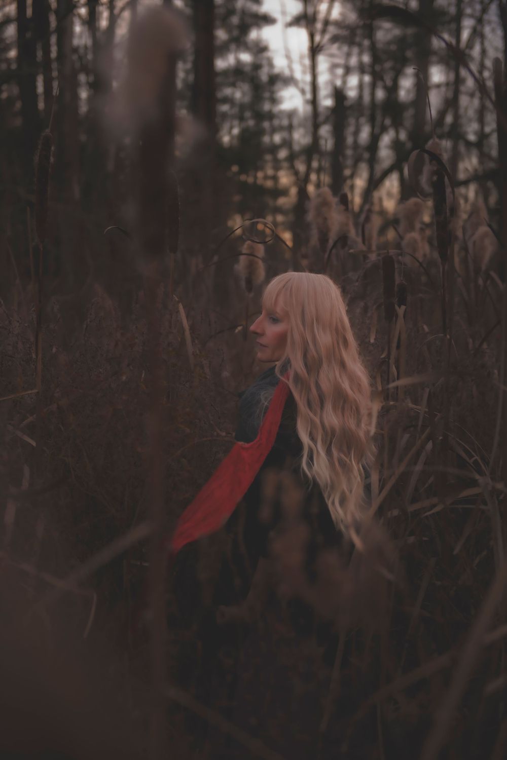 Dreamy forest portrait with flowing blonde hair and dark clothing against natural backdrop.