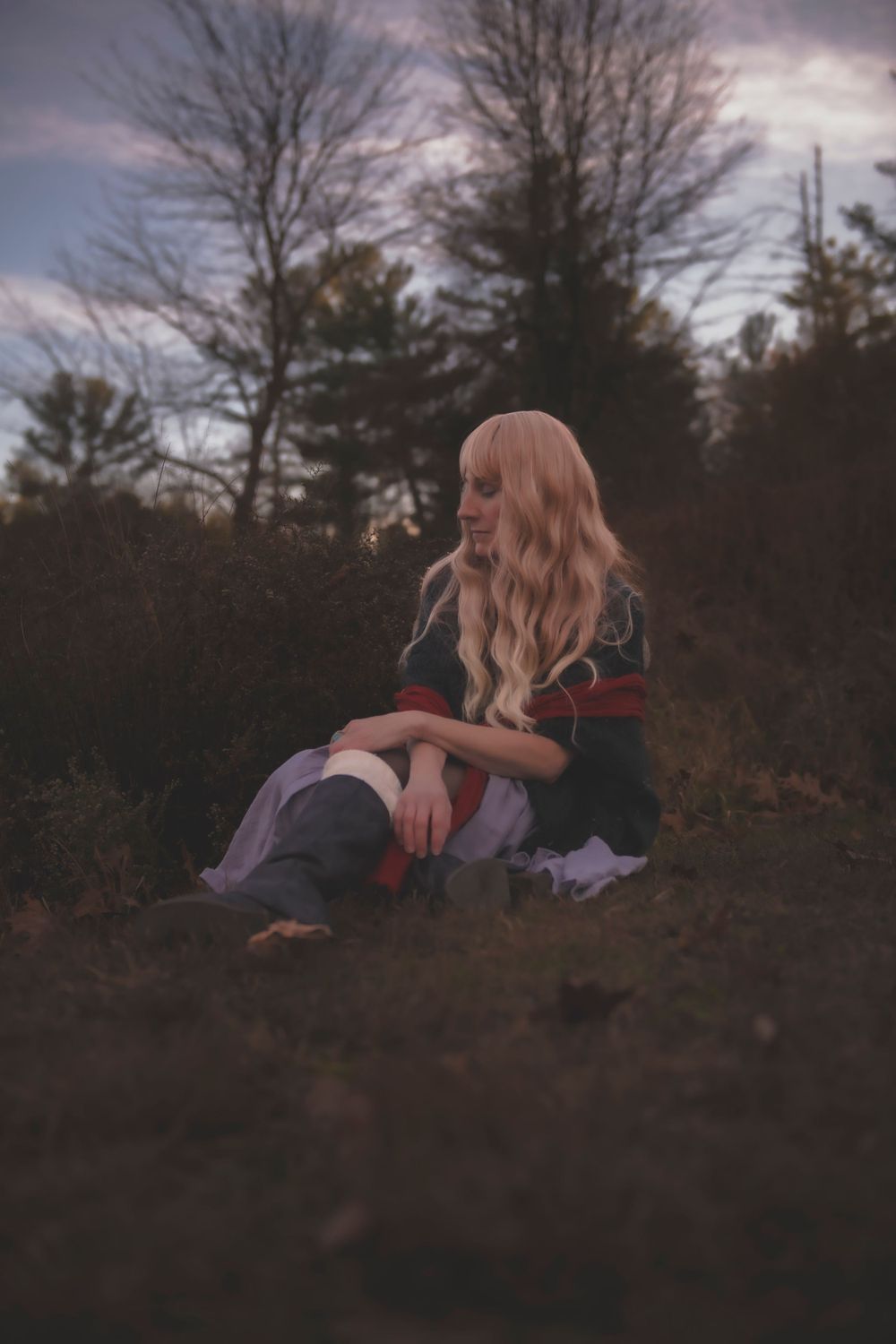 Dreamy forest portrait shows someone in vintage clothing sitting on ground at dusk.