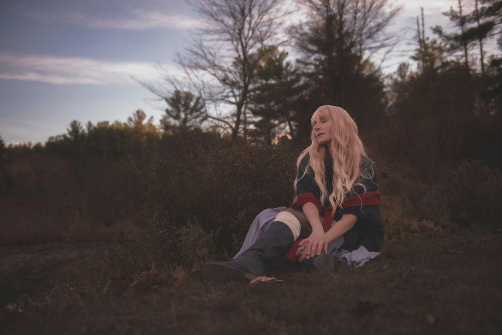 Atmospheric portrait of someone sitting on ground against twilight forest backdrop.