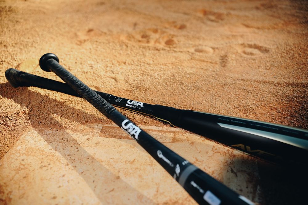 Two black baseball bats laying on sandy baseball diamond infield dirt.