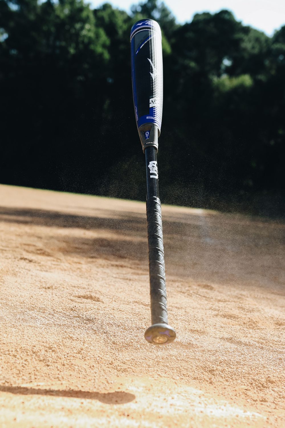 DeMarini baseball bat dropping into sandy infield dirt creating a dust cloud on a baseball field.