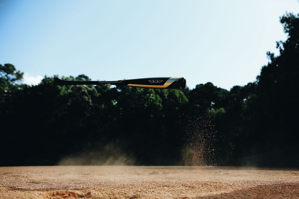 Yellow and black baseball bat flying through the air above a dusty baseball field infield dirt.