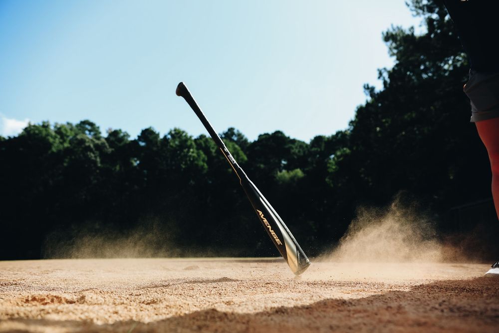 Baseball bat falling onto sandy infield dirt creating a large dust cloud on a sunny baseball field.