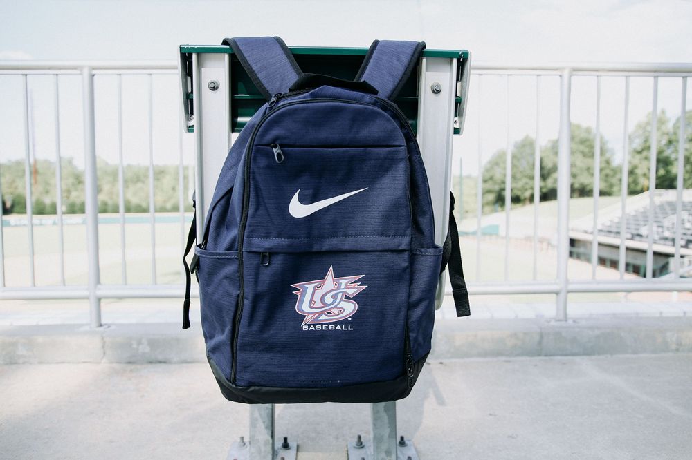 Navy blue Nike USA Baseball backpack displayed on stadium seating in outdoor ballpark.