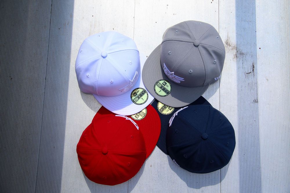 Four USA Baseball New Era fitted caps in white, red, gray, and navy arranged overhead.