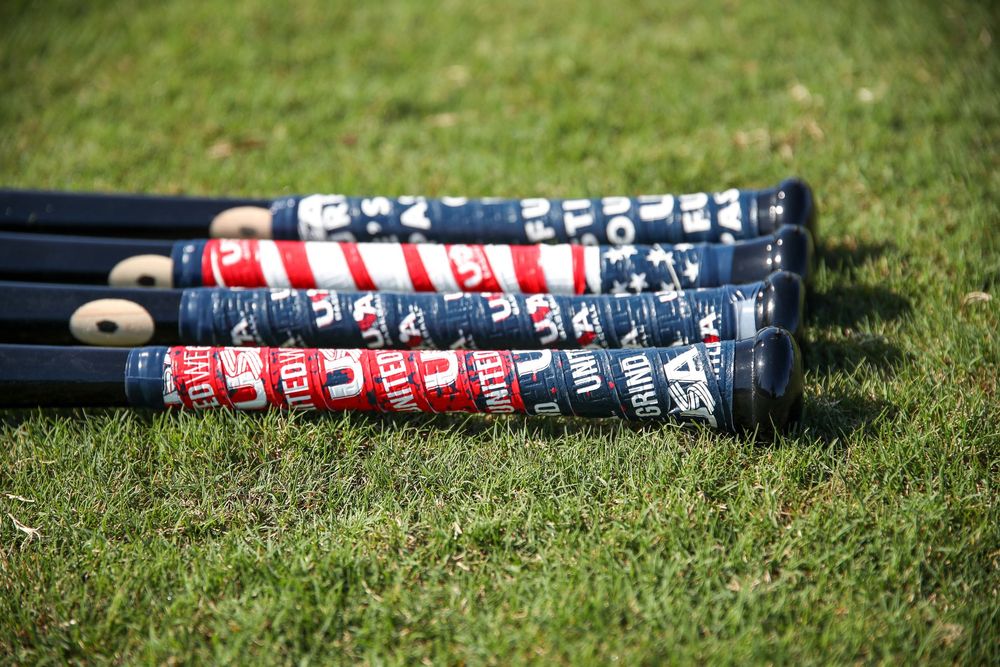 Four USA Baseball themed black bats with patriotic red, white, and blue grip tape lying on green grass.