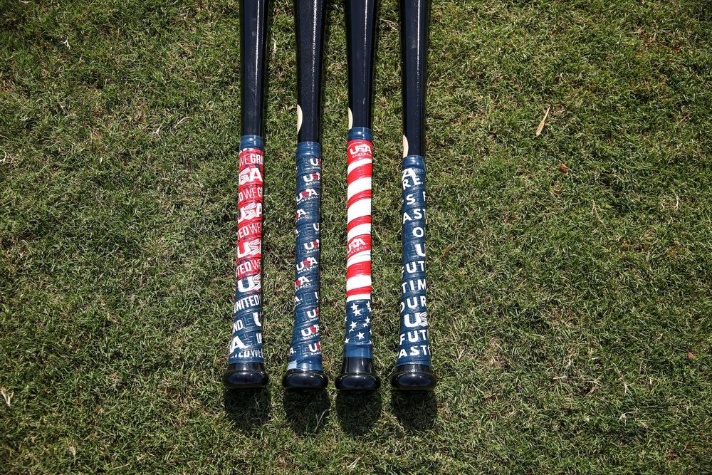 Close-up of four black baseball bats with USA Baseball branded red, white, and blue grip tape on grass.