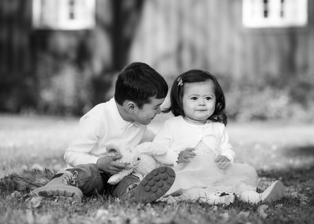 Black and white photo of two young children sitting together on grass in a quiet, vintage outdoor setting.