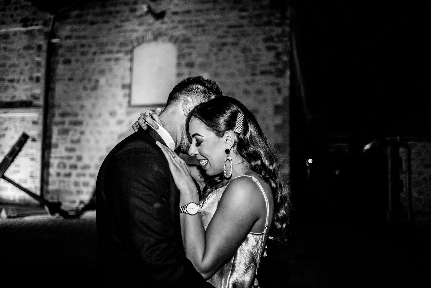 A couple dances romantically in the middle of a lamp-lit cobblestone street at night between historic buildings.