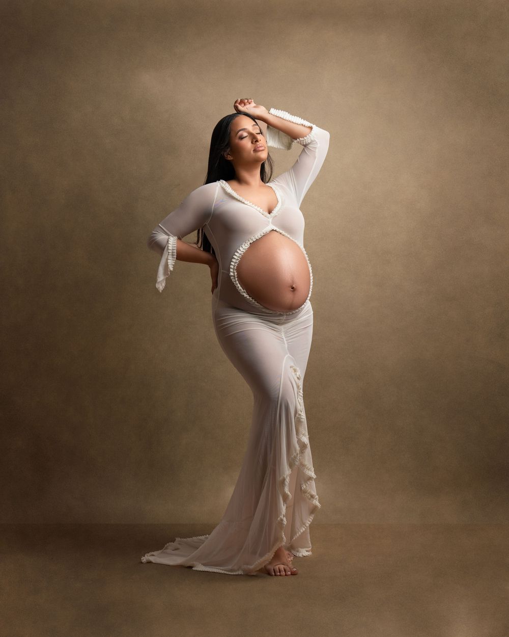 Graceful maternity pose in fitted white gown against neutral background.