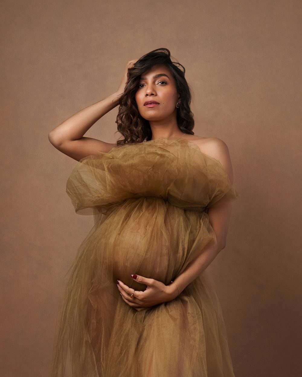 Studio maternity session with billowing gold tulle fabric creating ethereal floating effect.