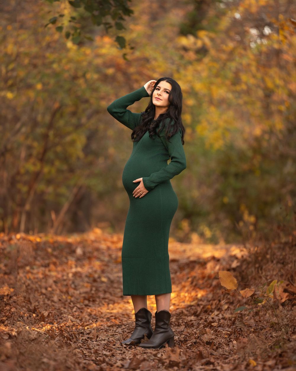 Outdoor maternity session featuring emerald green dress amid fall leaves and natural lighting.