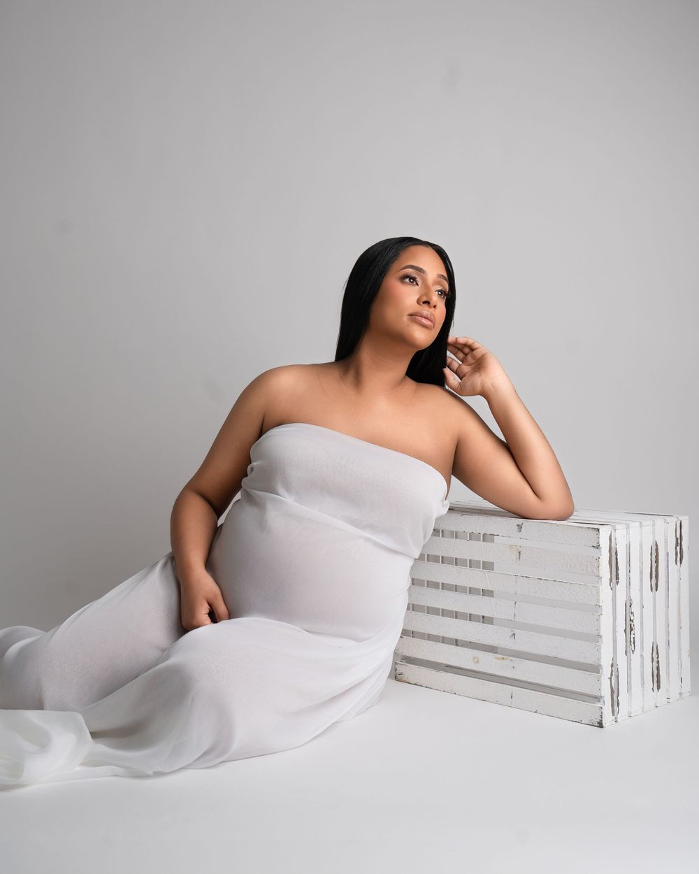 Contemporary maternity portrait with white dress and rustic wooden prop.