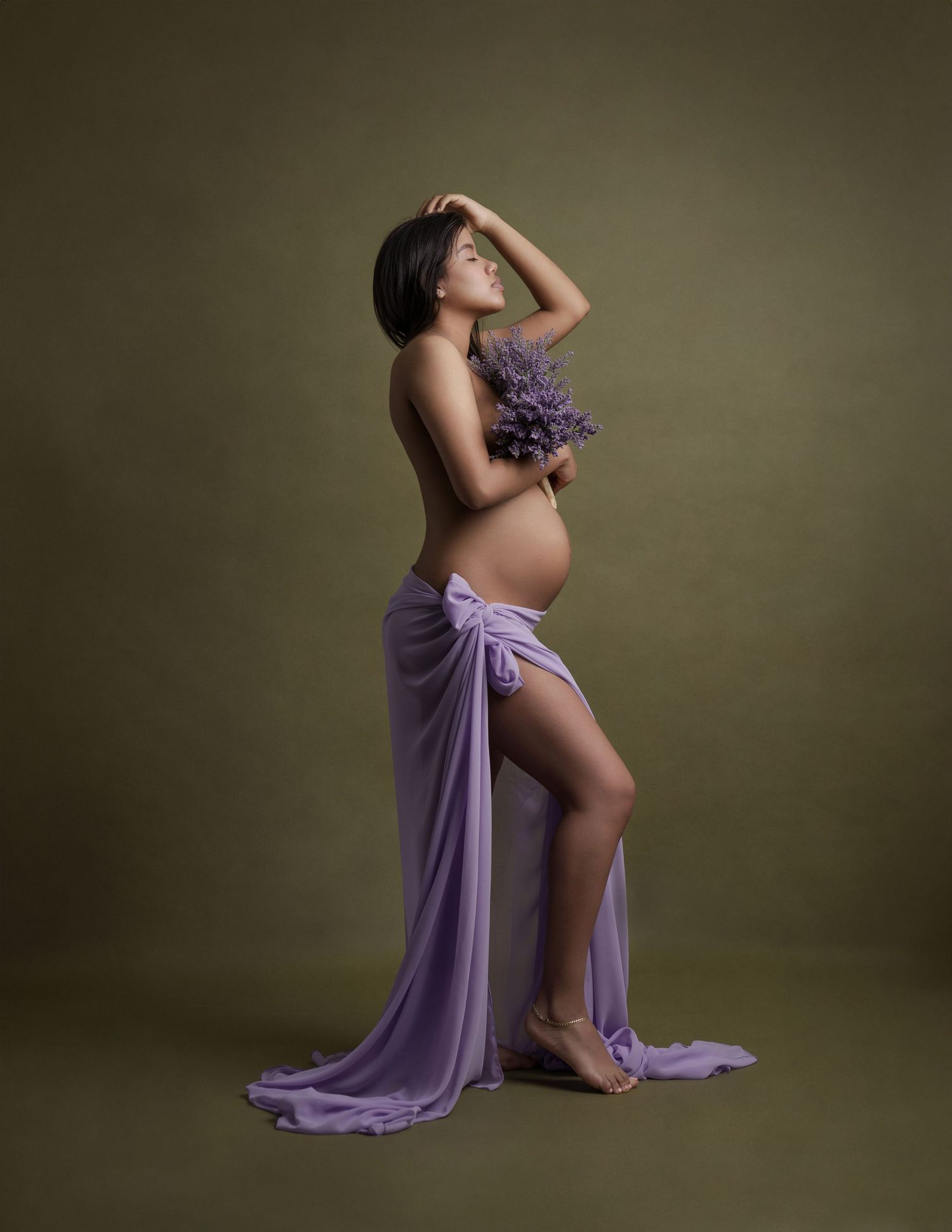 Elegant maternity portraits in purple flowing fabric against dark olive studio background.