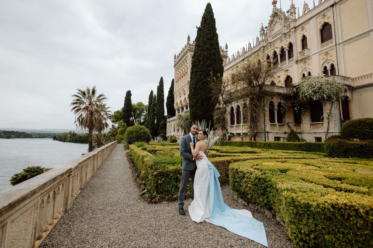 Elegant wedding couple walks along architectural archways at a Mediterranean villa with cypress trees and palm trees.