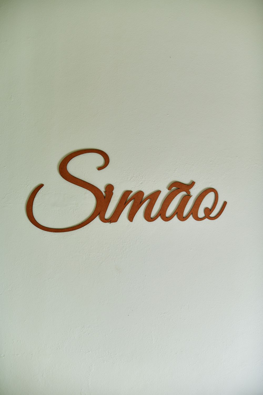A wooden laser-cut name sign reading Simao mounted on a white wall in cursive script.