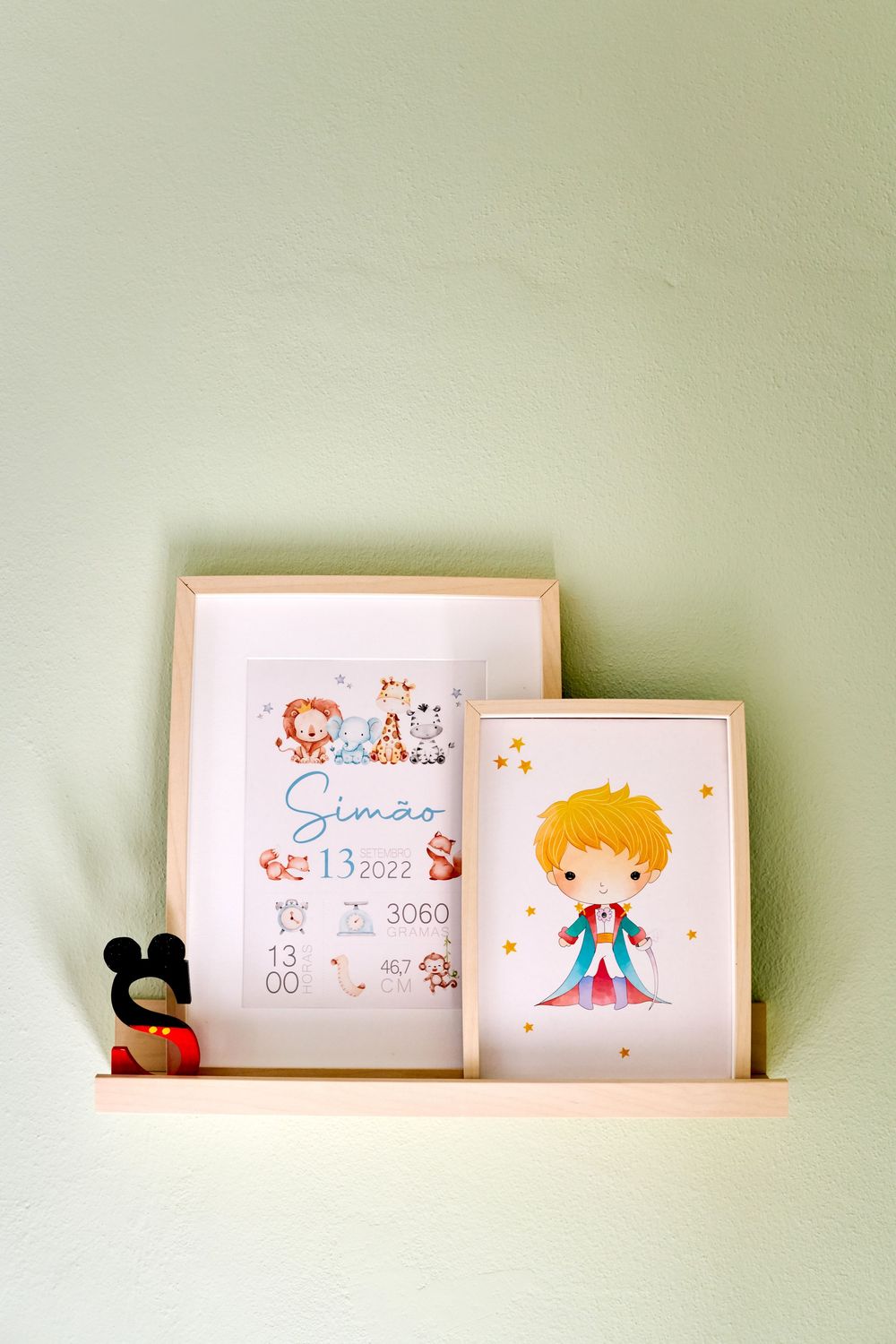 Two framed prints on a nursery shelf, one birth announcement for Simao and a Little Prince illustration.