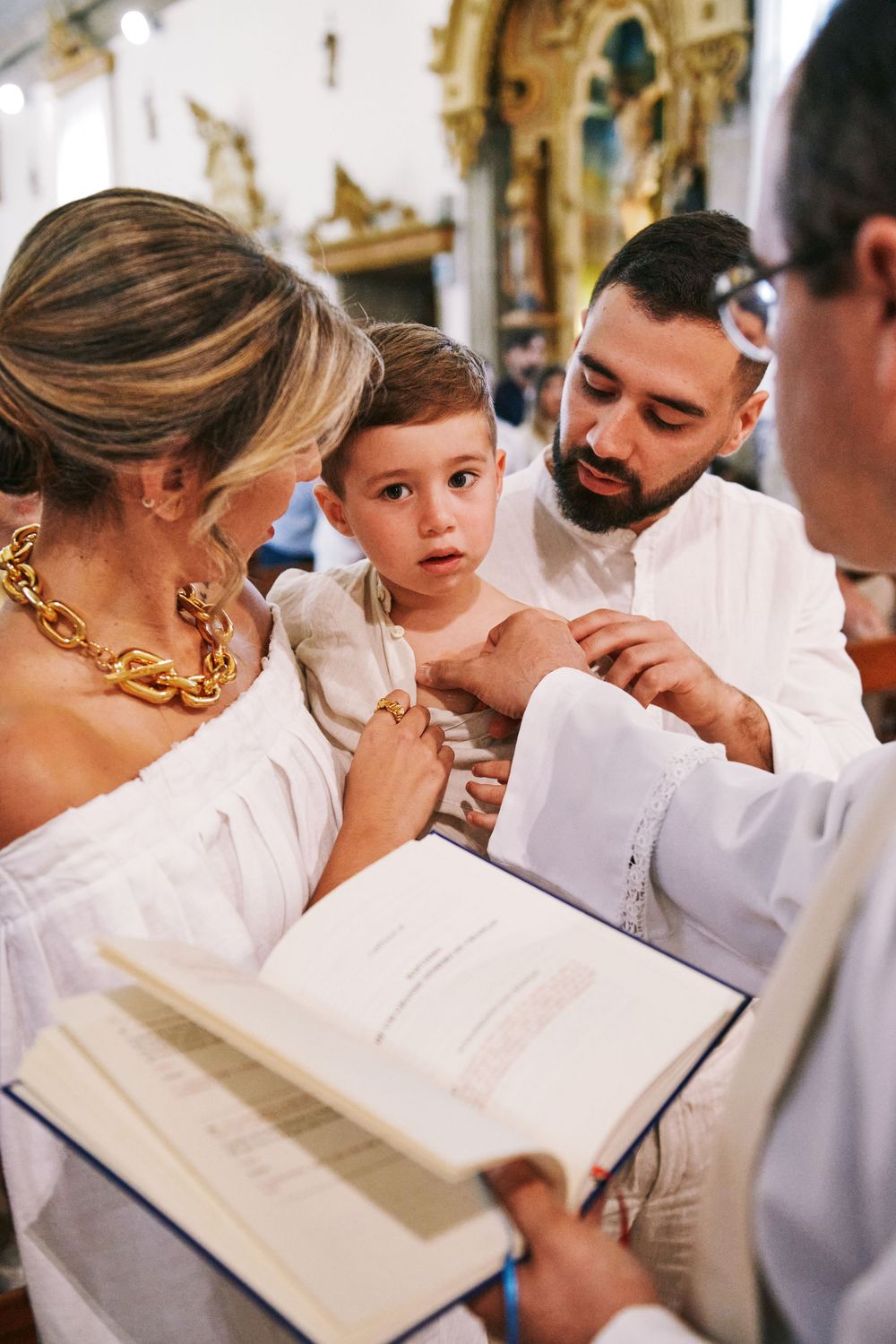 A priest reads from a book during a baptism ceremony as parents hold their infant in a church.