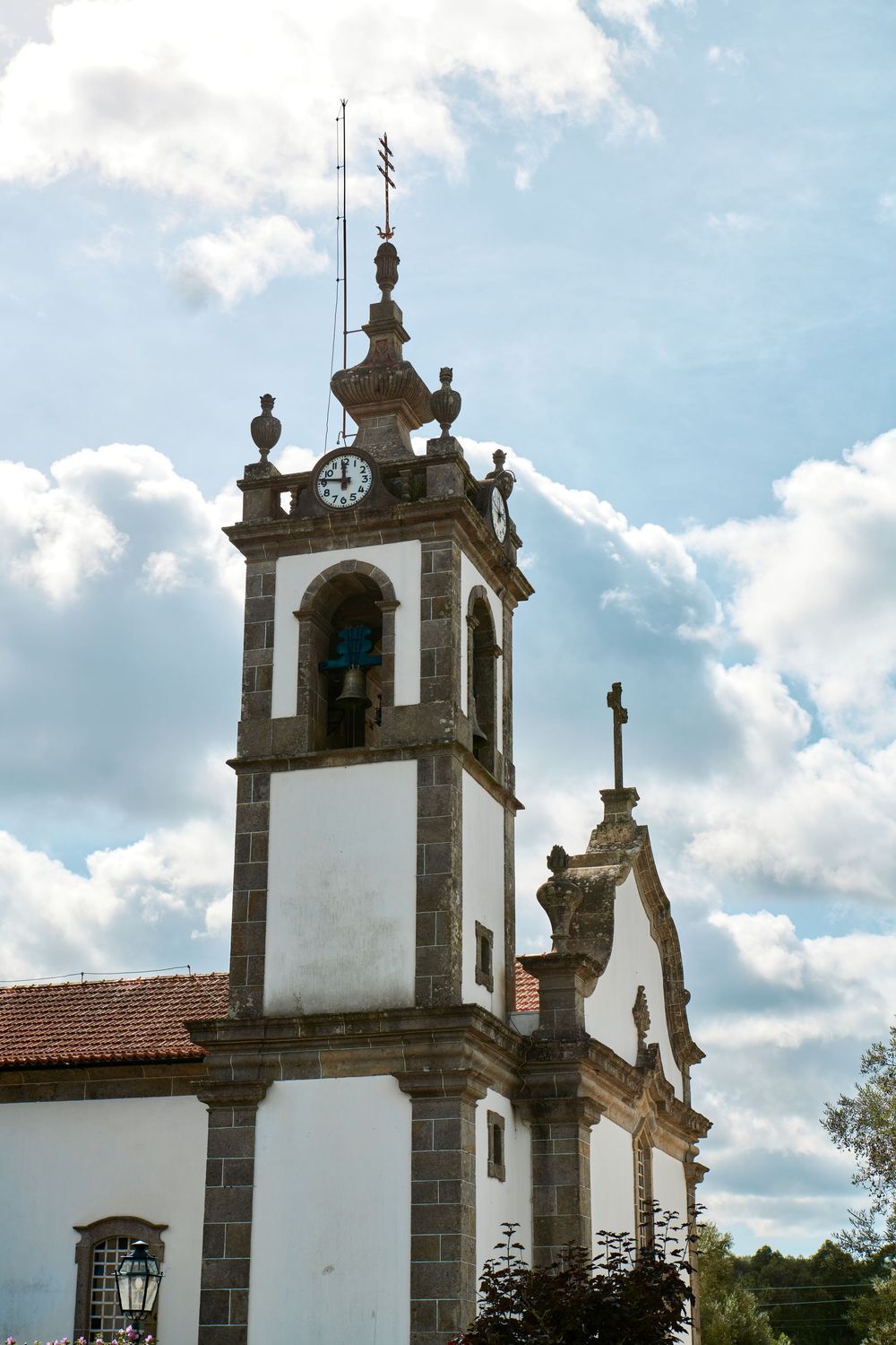 A traditional white and granite Portuguese church tower with clock against a partly cloudy blue sky.