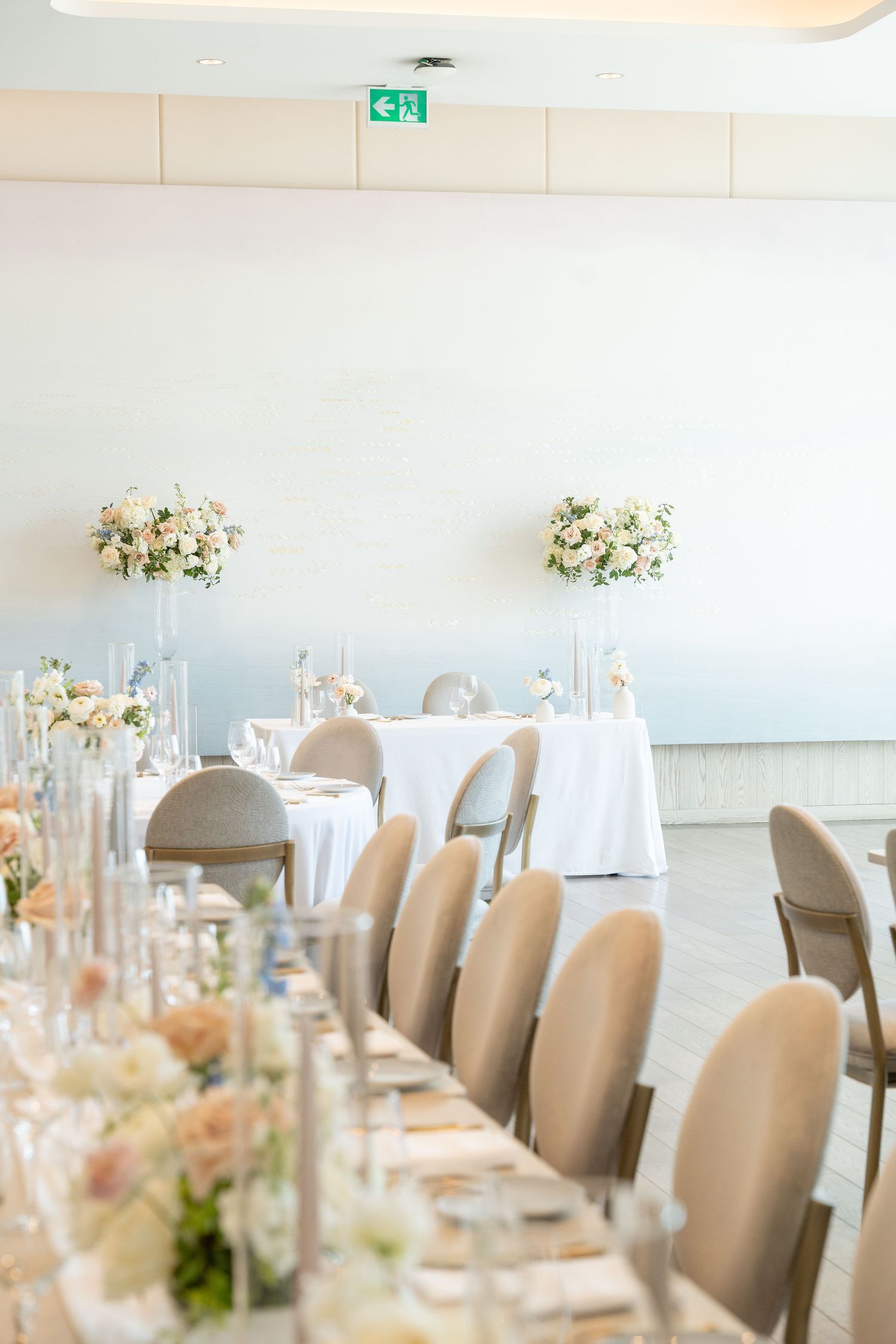 Elegant table setting with floral centerpieces and beige chairs in a bright dining space.