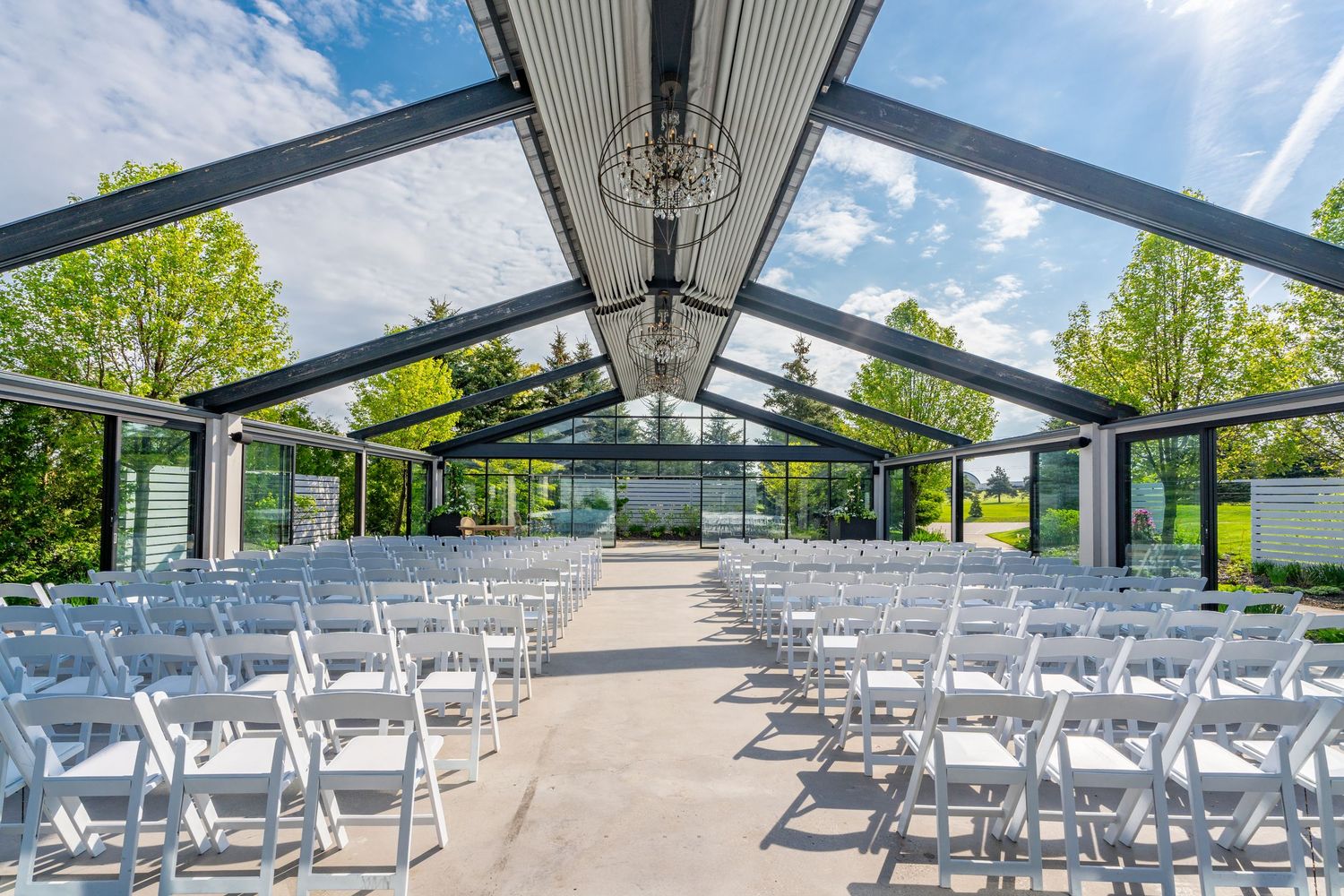 Outdoor ceremony space at Whistlebear Golf Club with white chairs set up under a glass-covered pavilion.