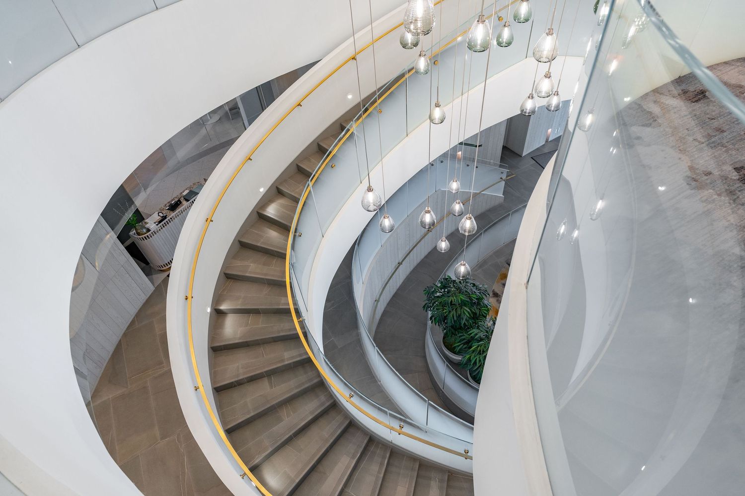 Modern curved staircase with glass railings and pendant lights in a luxury building interior.