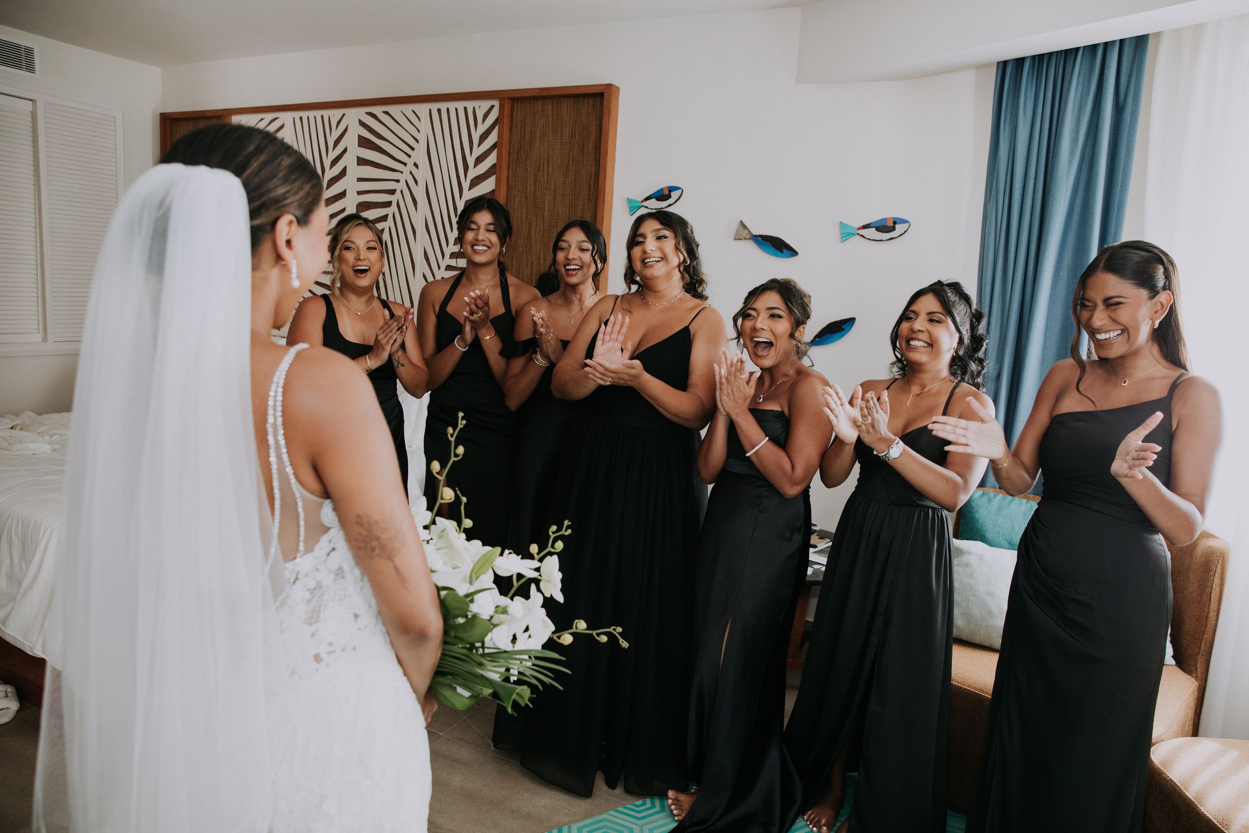 Bridesmaids in black dresses react emotionally to seeing bride in wedding dress for first time.
