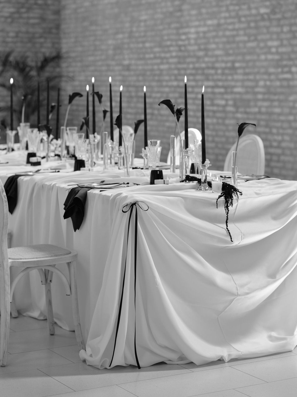 Elegant wedding table setting with white linens and tall black candles in a brick-walled venue. Photoshoot by Venice Photographer Alina Indi