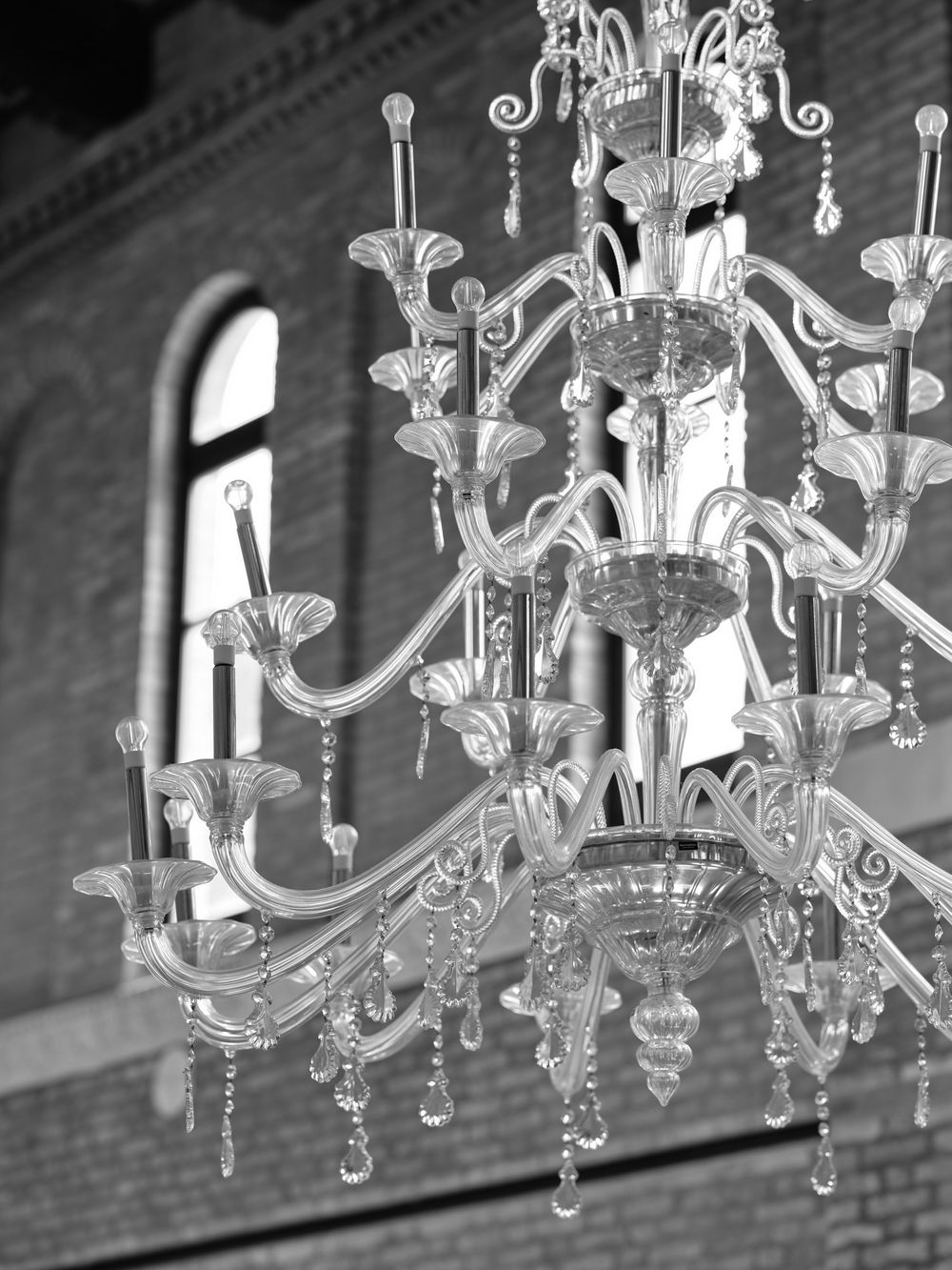 Ornate crystal chandelier with multiple tiers photographed in black and white against brick walls. Photoshoot by Venice Photographer