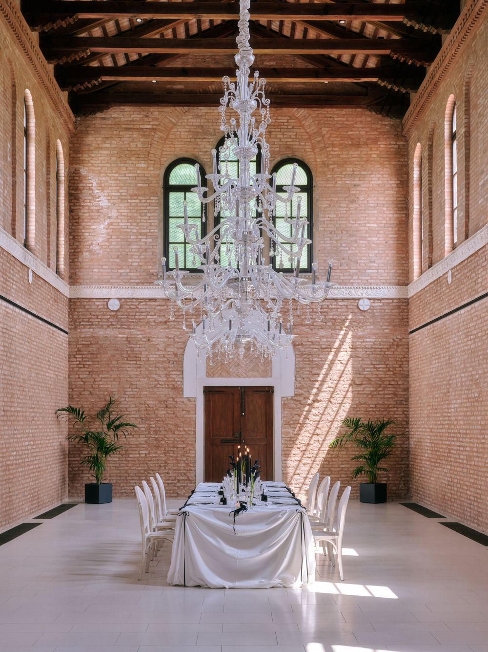 Spacious brick-walled venue with crystal chandeliers and white draping for an elegant event. Photoshoot by Venice Photographer Alina Indi