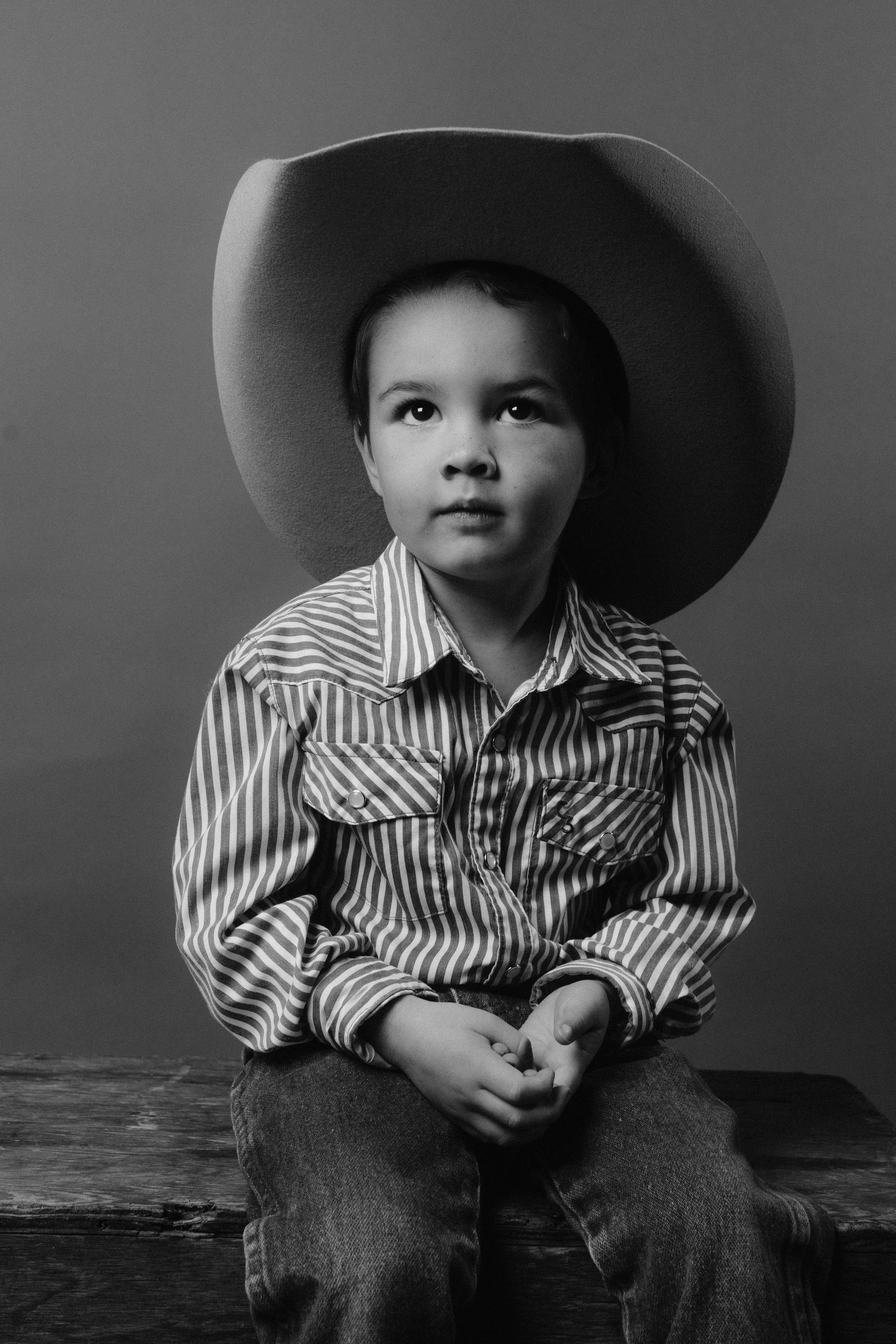 A black and white portrait of a young child wearing a cowboy hat and striped shirt.