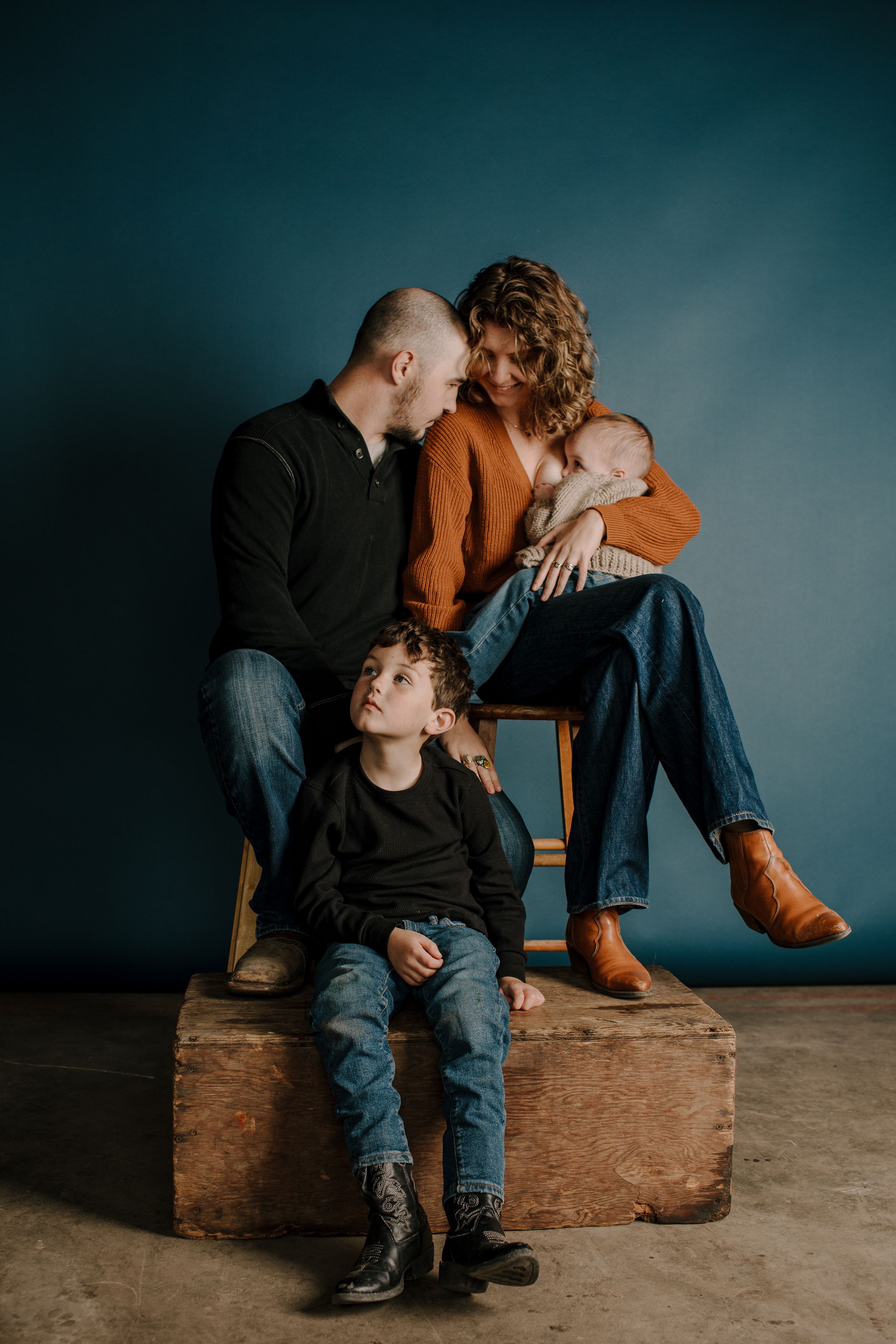 Family sitting together on wooden bench in moody studio setting.